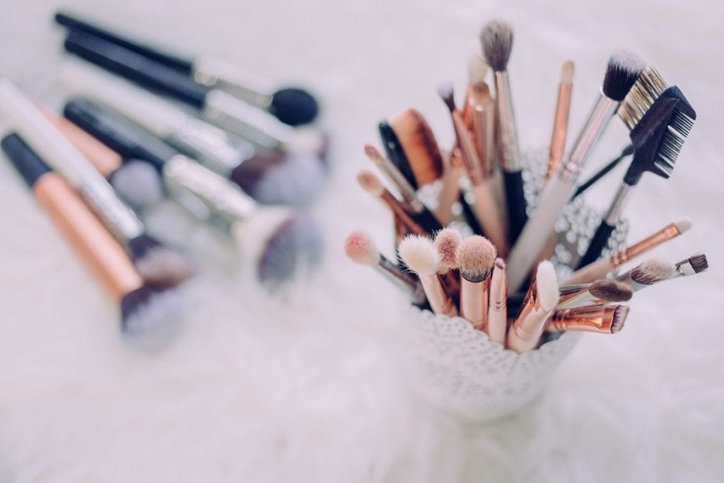 Makeup brushes and tools in a decorative glass holder, perfect for bridal or event makeup.