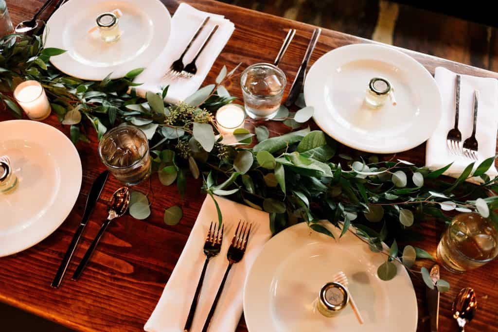 Elegant wedding table setting with greenery centerpiece, candles, and fine china for a romantic celebration.