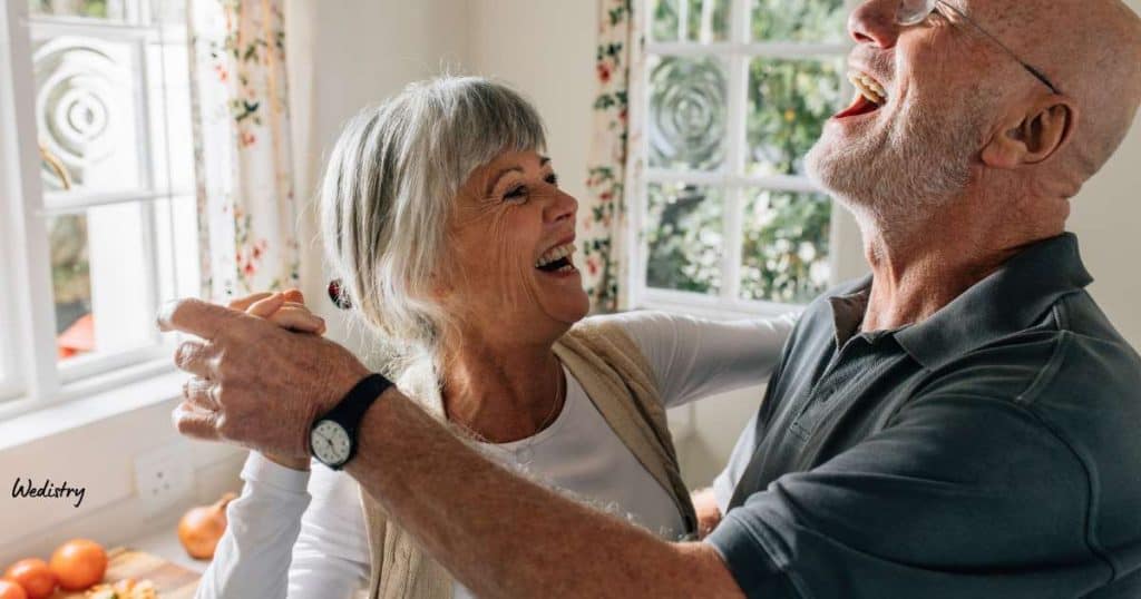 Joyful elderly couple dancing and laughing together during a happy moment at home.