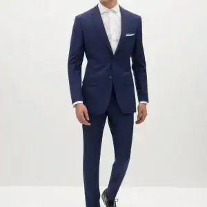 Elegant groom in navy blue wedding suit, chiffon shirt, and black shoes for wedding attire.